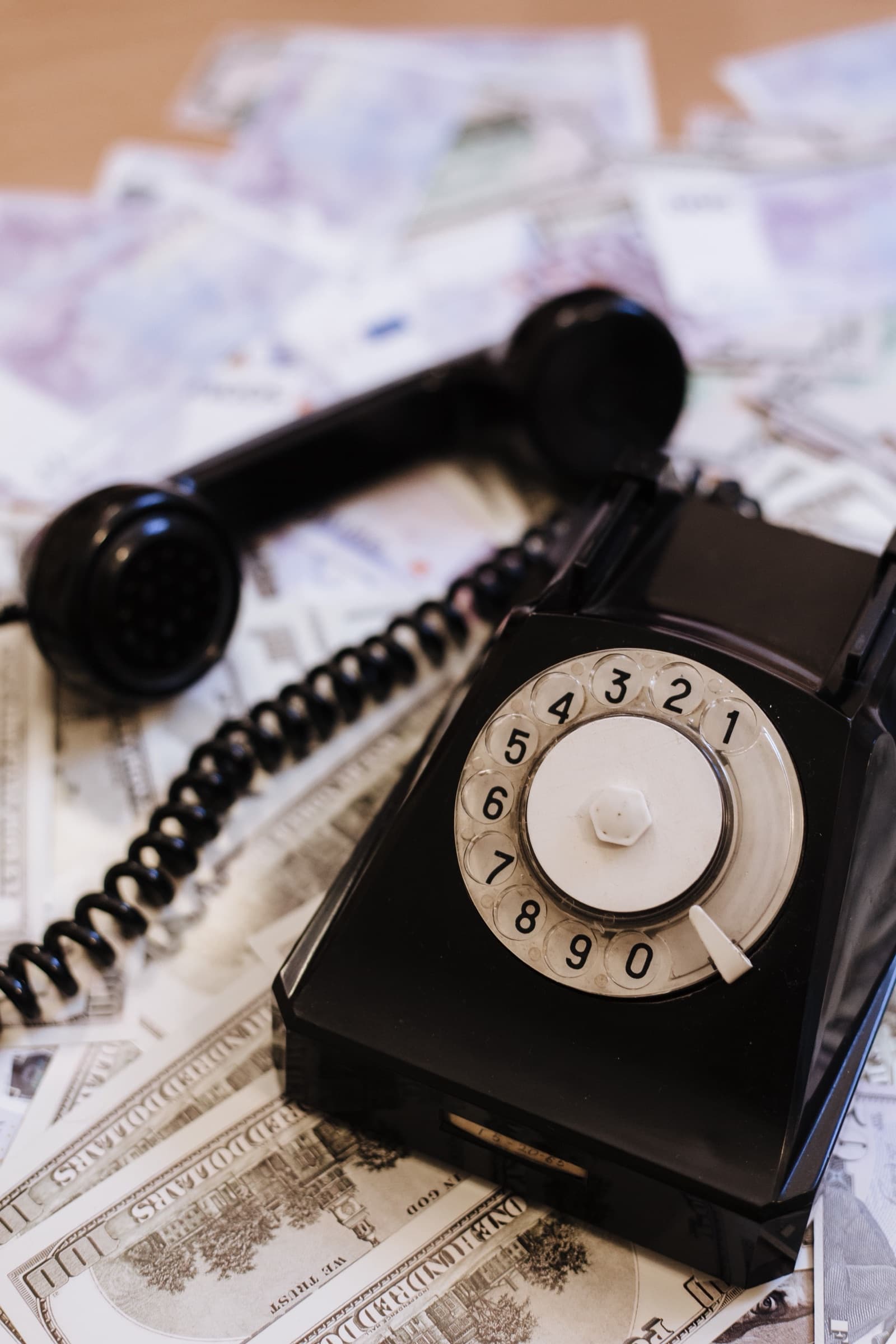 A black rotary dial telephone with its handset off the hook, resting on scattered dollar bills